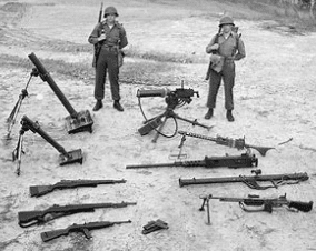 Two men standing in front of a pile of guns.
